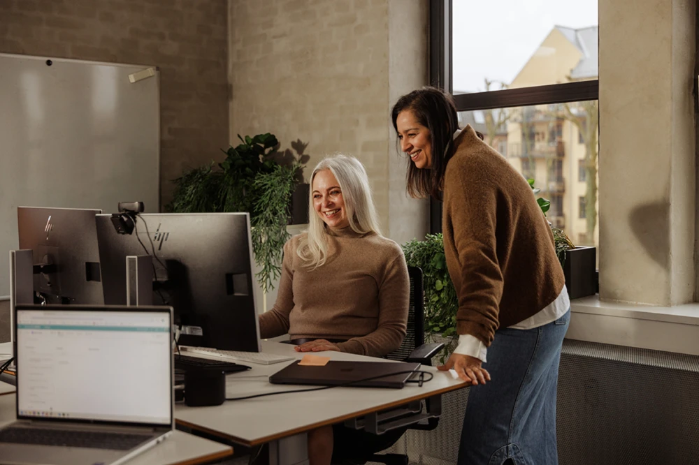 Manager assisting an employee at her desk while they look at the computer screen together.