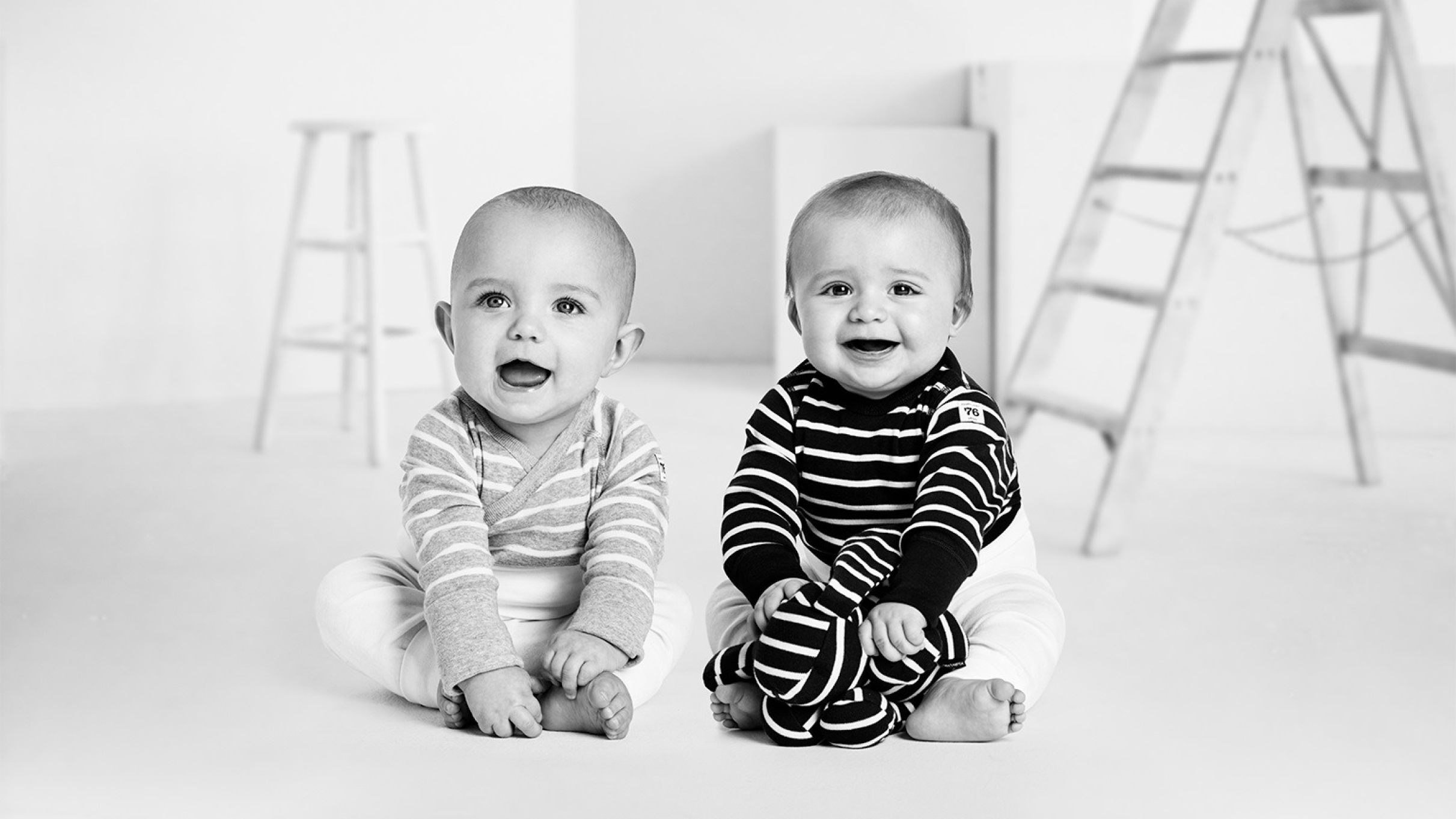 Two smiling babies sitting on the floor in a minimal black and white studio
