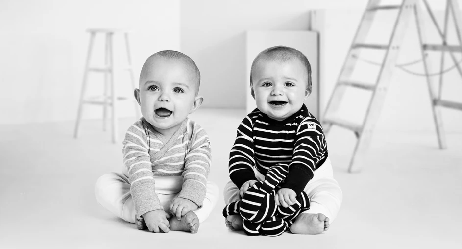 Two smiling babies sitting on the floor in a minimal black and white studio