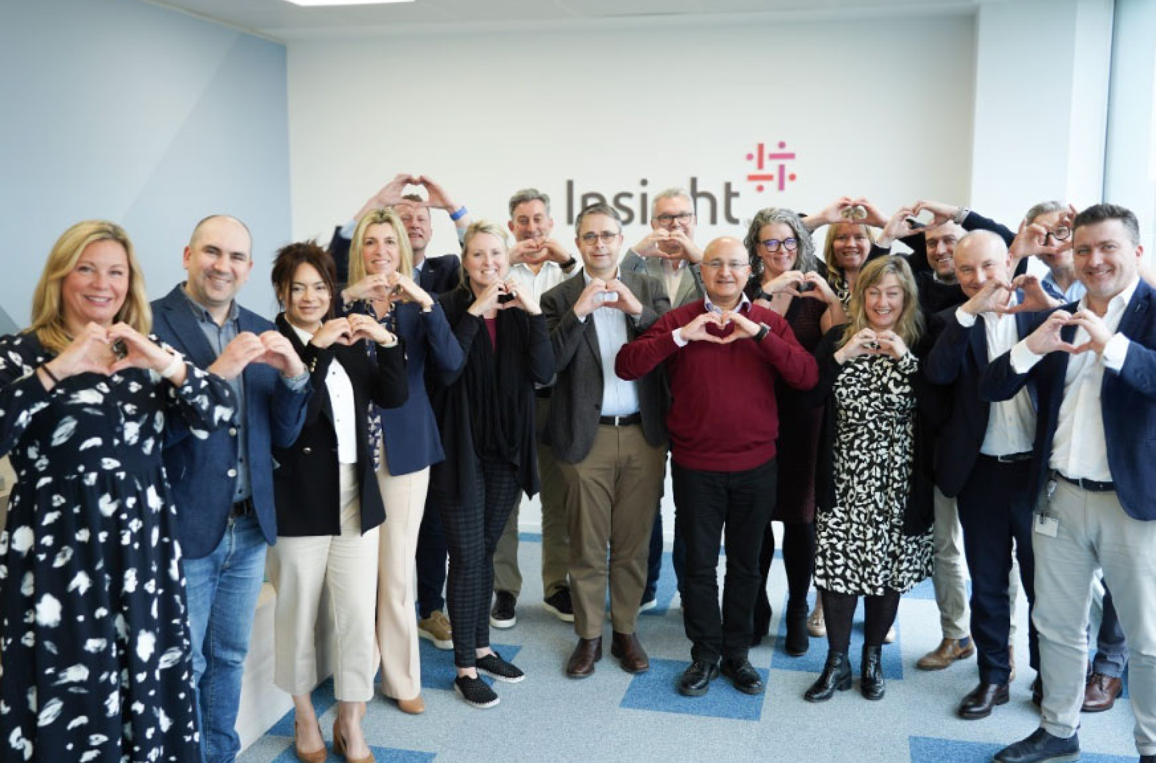 Insight team members smiling and making heart-hand gestures in front of a branded wall