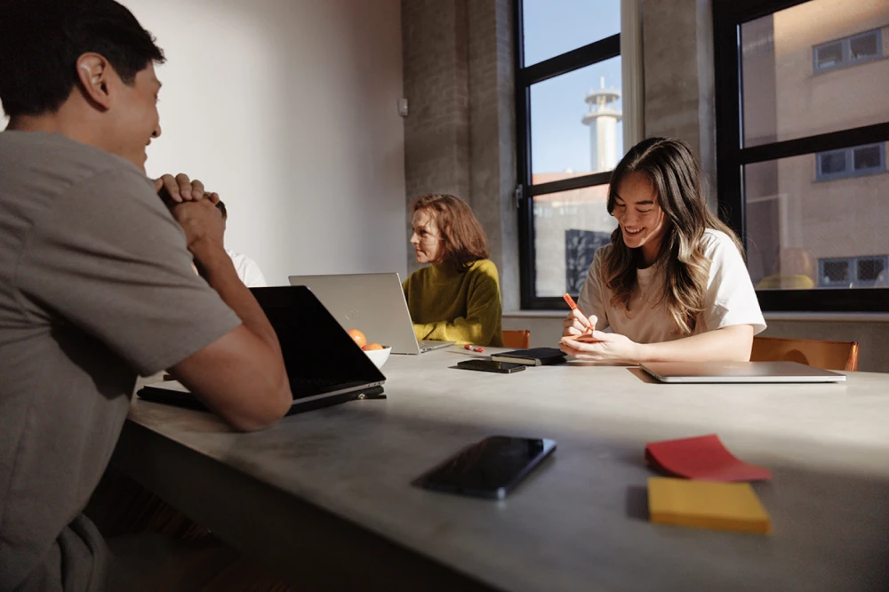 A smiling girl taking notes at a table during a meeting with her coworkers sitting near her